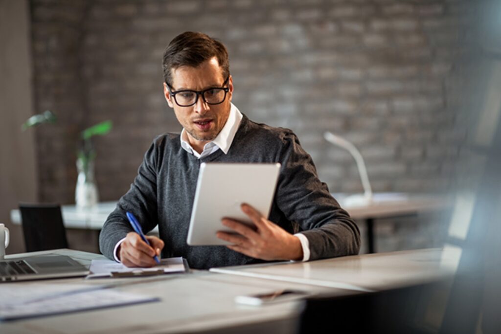 businessman using touchpad and taking notes on the paper.